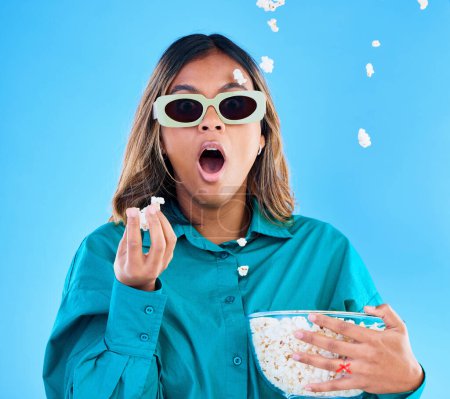 Photo for 3D movie, popcorn and surprise with a woman in studio on a blue background looking shocked while eating a snack. Portrait, glasses and wow with an attractive young female watching video entertainment. - Royalty Free Image