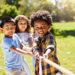 Fun, games and kids playing tug of war together outdoor in a park or playground in summer. Friends, diversity and children pulling a rope while being playful fun or bonding in a garden on a sunny day.