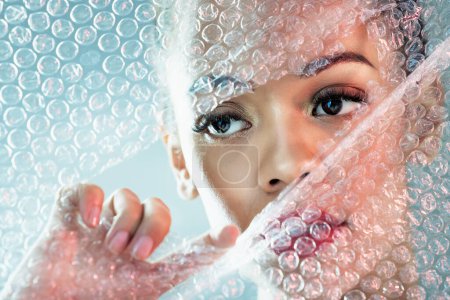 Photo for Bubble wrap, cosmetics and face of woman with makeup, red lipstick and skincare products in studio. Creative art, beauty mockup and girl with facial glow, aesthetic and luxury style with plastic tear. - Royalty Free Image