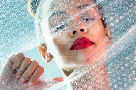 Photo for Beauty, bubble wrap and makeup with breakthrough with woman for package, creative and cosmetics. Plastic, confidence and face with female model and red lipstick for facial, art and glow in studio. - Royalty Free Image