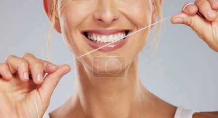 Zahnseide, Zahnwellness und eine lächelnde Frau beim Mundputzen vor grauem Studiohintergrund. Modellhände mit Schnur zur Pflege der Zahngesundheit und Mundgesundheit mit Lächeln.