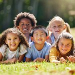 Portrait, smile and children lying on grass in nature on vacation outdoor for learning. Kids, diversity and happiness of group enjoying summer holiday at park or garden, bonding or relaxing together