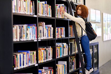 Téléchargez les photos : Atteindre la connaissance. une jeune femme cherchant un livre dans une bibliothèque universitaire - en image libre de droit