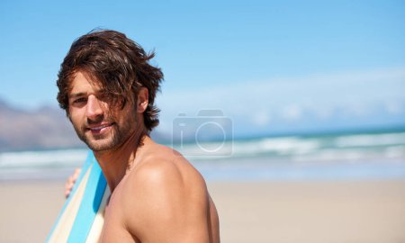 Hes ready to surf. A young man leaning on his surfboard looking at the camera