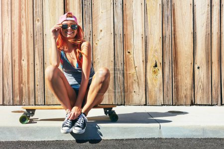 Photo for Who cares what people think. a young woman sitting on her skateboard on a sidewalk - Royalty Free Image