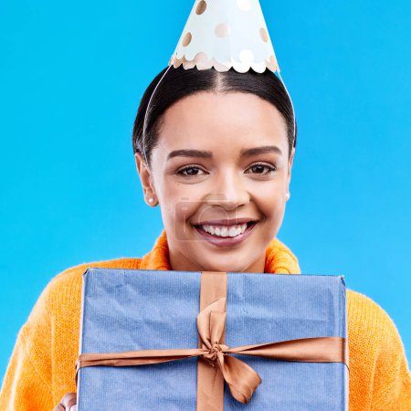 Woman, birthday and box in studio portrait with smile, happiness and present by blue background. Girl, model and party with gift, hat and excited face for celebration, event and package by backdrop.