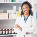 Pharmacy, pharmacist or portrait of woman with arms crossed or smile in customer services or clinic. Healthcare help desk, wellness or happy doctor smiling by medication on shelf in drugstore.
