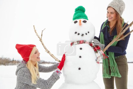 Téléchargez les photos : Tu veux construire un bonhomme de neige ? deux amis construisant un bonhomme de neige ensemble - en image libre de droit