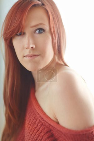 Photo for Portrait of one beautiful young redhead woman relaxing home. Confident female feeling flirty, sensual and sexy while posing seductively a warm jersey exposing her shoulder and looking seductive. - Royalty Free Image