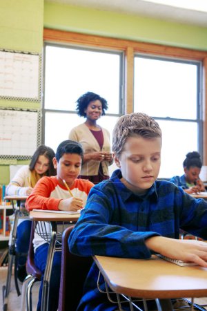 Téléchargez les photos : L'évaluation est une étape cruciale du processus d'apprentissage. un jeune garçon assis en classe avec son professeur et ses camarades de classe brouillés en arrière-plan - en image libre de droit