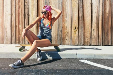 Photo for Skaters have more fun. a young woman sitting on her skateboard on a sidewalk - Royalty Free Image