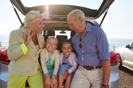 Photo for Getaway with the grandkids. two little girls sitting in the trunk of a car with their grandparents - Royalty Free Image
