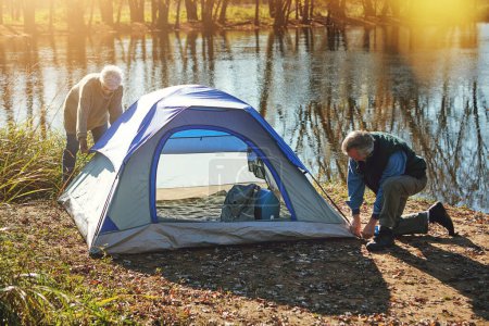 Téléchargez les photos : C'est l'endroit idéal pour installer un camp. un couple de personnes âgées installant une tente tout en campant dans le désert - en image libre de droit
