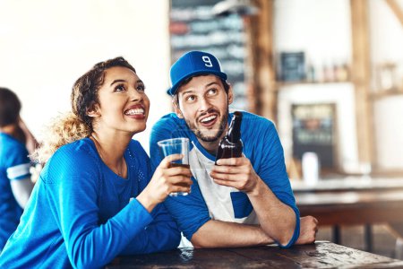 Téléchargez les photos : Le jeu qui les a rapprochés. un jeune homme et une jeune femme qui boivent des bières en regardant un match de sport dans un bar - en image libre de droit
