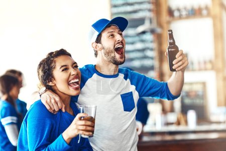Téléchargez les photos : Des âmes sœurs fans de sport. un jeune homme et une jeune femme qui boivent des bières en regardant un match de sport dans un bar - en image libre de droit