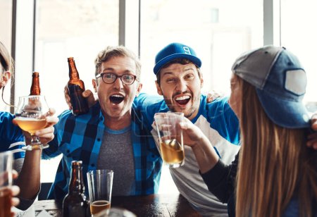 Téléchargez les photos : Ensemble au nom du jeu. un groupe d'amis buvant des bières en regardant un match de sport dans un bar - en image libre de droit