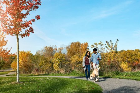 Foto de Nada mejor que caminar con nuestro niño de cuatro patas. una pareja joven y cariñosa llevando a su perro a dar un paseo por el parque - Imagen libre de derechos