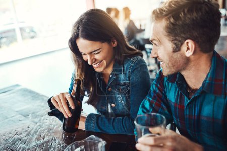 Téléchargez les photos : Ses histoires la font piquer. un jeune homme et une jeune femme heureux qui boivent des bières dans un bar - en image libre de droit