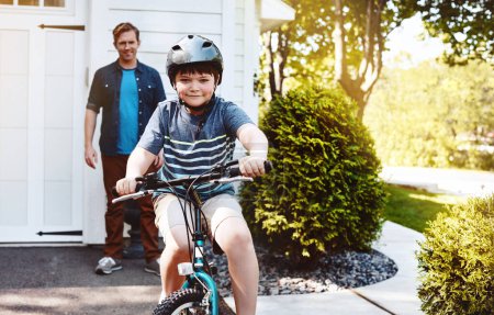Téléchargez les photos : C'est facile une fois que vous y allez. un jeune garçon en vélo avec son père en arrière-plan - en image libre de droit