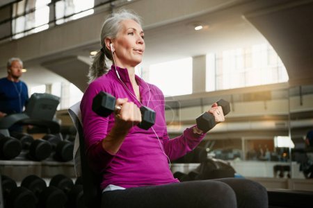 Téléchargez les photos : Respirer correctement est essentiel pour la forme physique. Portrait d'une femme âgée travaillant avec des poids au gymnase - en image libre de droit