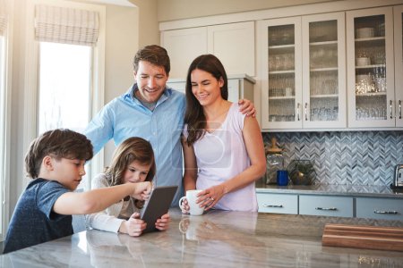 Téléchargez les photos : S'entraider au niveau suivant du jeu. un couple marié et leurs jeunes enfants jouant avec une tablette ensemble dans leur cuisine - en image libre de droit
