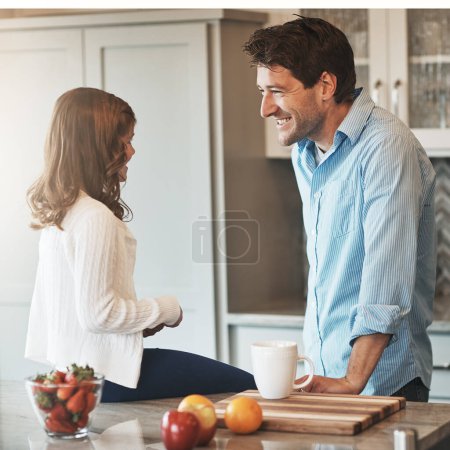 Téléchargez les photos : Discuter avec sa personne préférée. une petite fille heureuse bavardant avec son père assis sur le comptoir de la cuisine à la maison - en image libre de droit