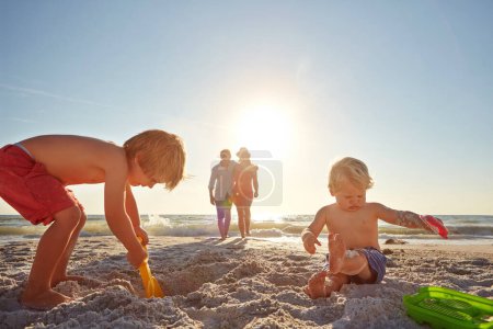 Foto de Divirtiéndose un poco. dos niños pequeños jugando en la playa con sus padres en el fondo - Imagen libre de derechos