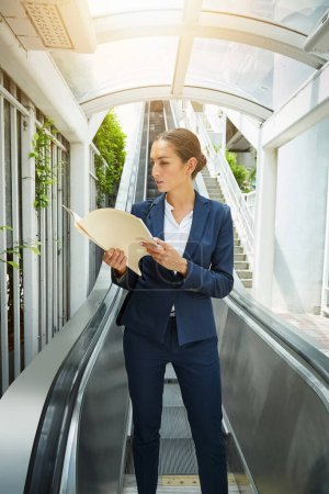 Photo for Theres always time for paperwork. a young businesswoman reading paperwork on an escalator - Royalty Free Image