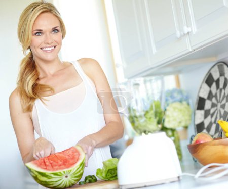 Photo for Getting ready to make the perfect smoothie. Attractive blonde woman slicing a watermelon in her kitchen at home - Royalty Free Image