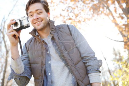 Foto de Sacando tantas fotos hermosas. Un joven tomando fotografías en un día de otoño en un bosque con su cámara y sonriendo - Imagen libre de derechos