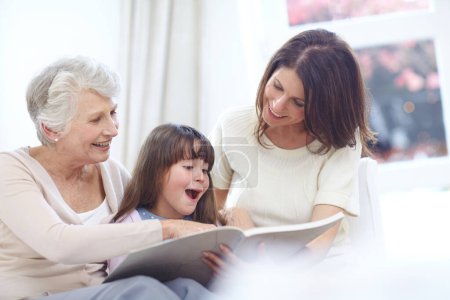 Téléchargez les photos : Et ils ont vécu heureux pour toujours... une petite fille assise avec sa mère et sa grand-mère et lisant un livre - en image libre de droit