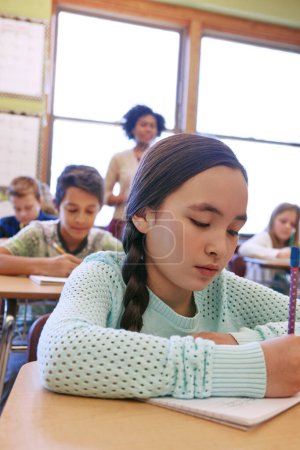 Photo for She studied hard for this test. a young girl sitting in class with her teacher and classmates blurred in the background - Royalty Free Image