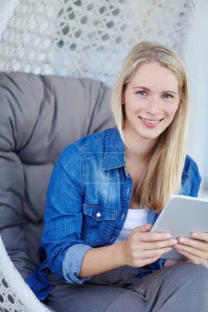 Staying in touch has never been easier. Portrait of a young woman using a digital tablet while relaxing in a hanging basket chair Poster 654110878