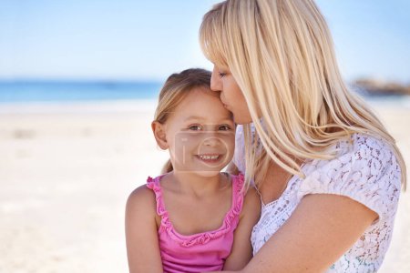 Foto de La niñita de mamá. Una madre cariñosa dándole a su hija un beso en la frente mientras está en la playa - Imagen libre de derechos