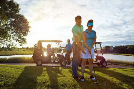 Foto de Eres natural, nena. un marido ayudando a su esposa a jugar al golf - Imagen libre de derechos