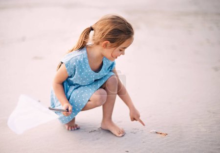 Téléchargez les photos : La curiosité des enfants. curieuse petite fille pointant quelque chose dans le sable - en image libre de droit