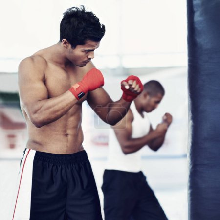 Photo for Hes dedicated to the sport of boxing. a young male boxers training on heavy bags - Royalty Free Image