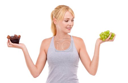 Foto de A veces es difícil tomar la decisión saludable. una joven mujer eligiendo entre un panecillo y algunas uvas - Imagen libre de derechos