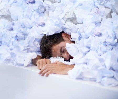Foto de Dejar que su trabajo lo consuma. un hombre de negocios enterrado bajo un montón de papeleo arrugado - Imagen libre de derechos
