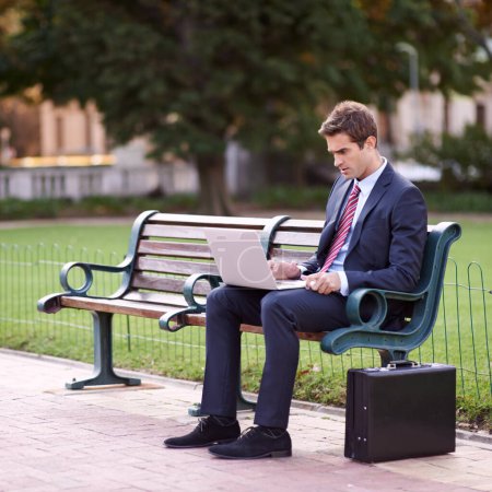 Photo for Park bench office. a handsome businessman working on his laptop while sitting on a park bench - Royalty Free Image