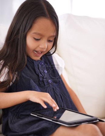 Téléchargez les photos : Grandir à l'ère numérique. une petite fille utilisant une tablette assise sur le canapé à la maison - en image libre de droit