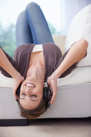 Photo for Lost in the music. A young woman lying upside down listening to music over her headphones - Royalty Free Image