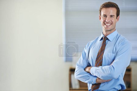 Téléchargez les photos : Monter l'échelle de l'entreprise. Un jeune homme d'affaires debout et souriant les bras croisés - copyspace - en image libre de droit