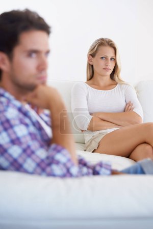 Foto de Es difícil de comprender - problemas de relación. Una mujer molesta sentada en un sofá con los brazos cruzados y mirando a su novio sentado en primer plano - Imagen libre de derechos
