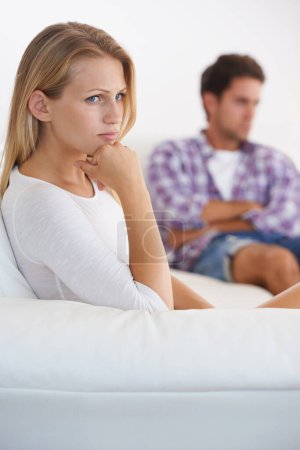 Foto de Dándole el tratamiento silencioso. Una mujer molesta sentada en un sofá e ignorando a su novio sentado en el fondo - Imagen libre de derechos