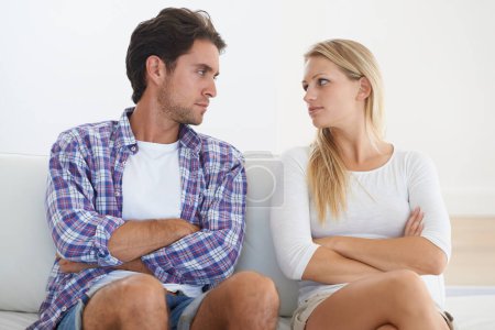 Confrontational couple - relationship issues. A disagreeing couple sitting on a couch together with arms crossed and looking at each other with upset
