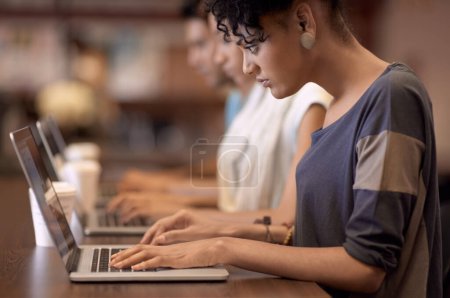 Téléchargez les photos : Dynamique des groupes d'étude. une jeune femme studieuse travaillant sur son ordinateur portable avec des personnes floues en arrière-plan - en image libre de droit
