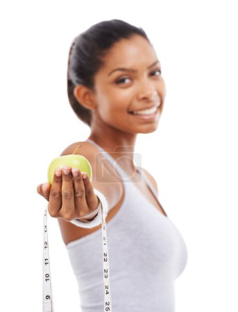 Photo for Make the healthy choice. A pretty young woman offering you an apple and a measuring tape while isolated on a white background - Royalty Free Image