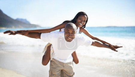 Photo for Together they soar. A handsome african-american man giving his girlfriend a piggyback on the beach - Royalty Free Image