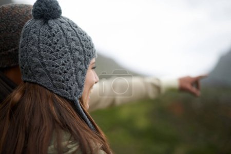 Téléchargez les photos : J'apprécie la vue. Une jeune femme debout dehors pointant quelque chose sur un jour froid d'hiver - en image libre de droit